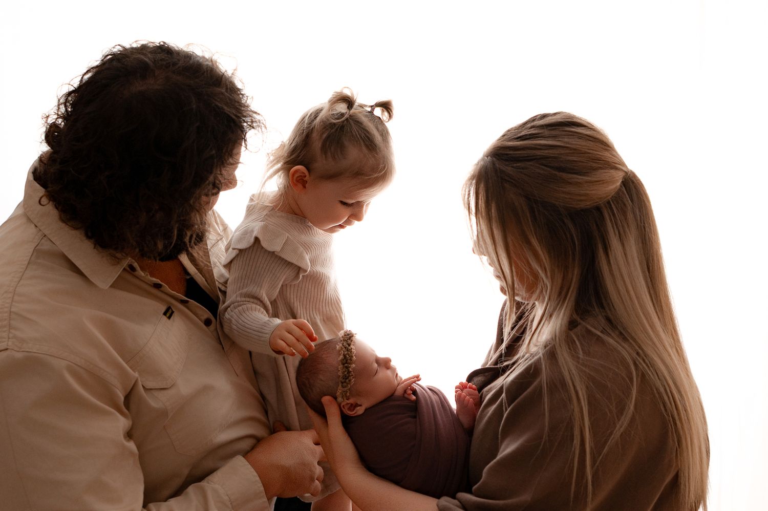 Family of four with two adults admiring a newborn baby held by a woman with long blonde hair.