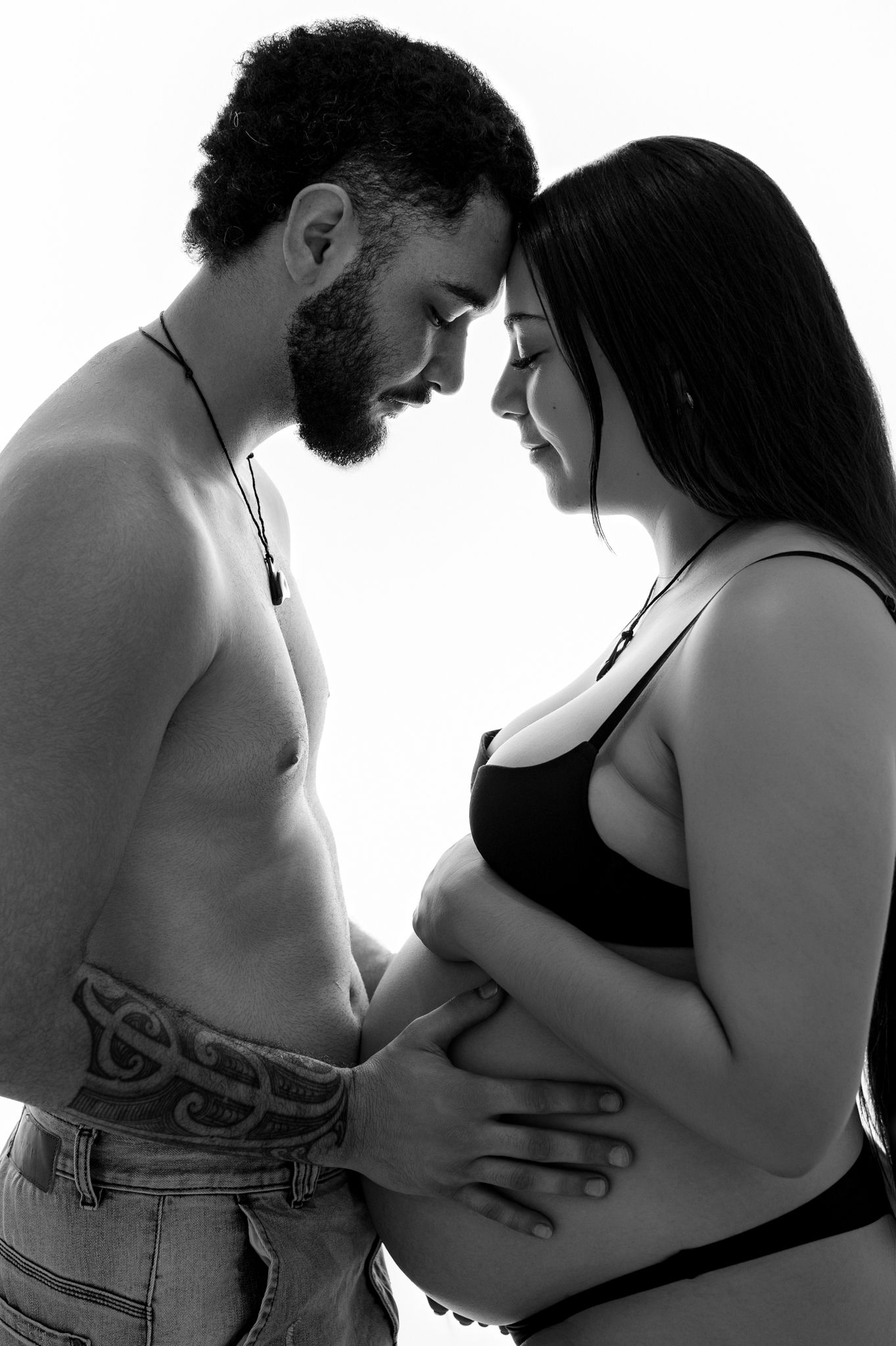 Artistic black and white maternity photo showing intimate moment between couple with focus on pregnant belly.