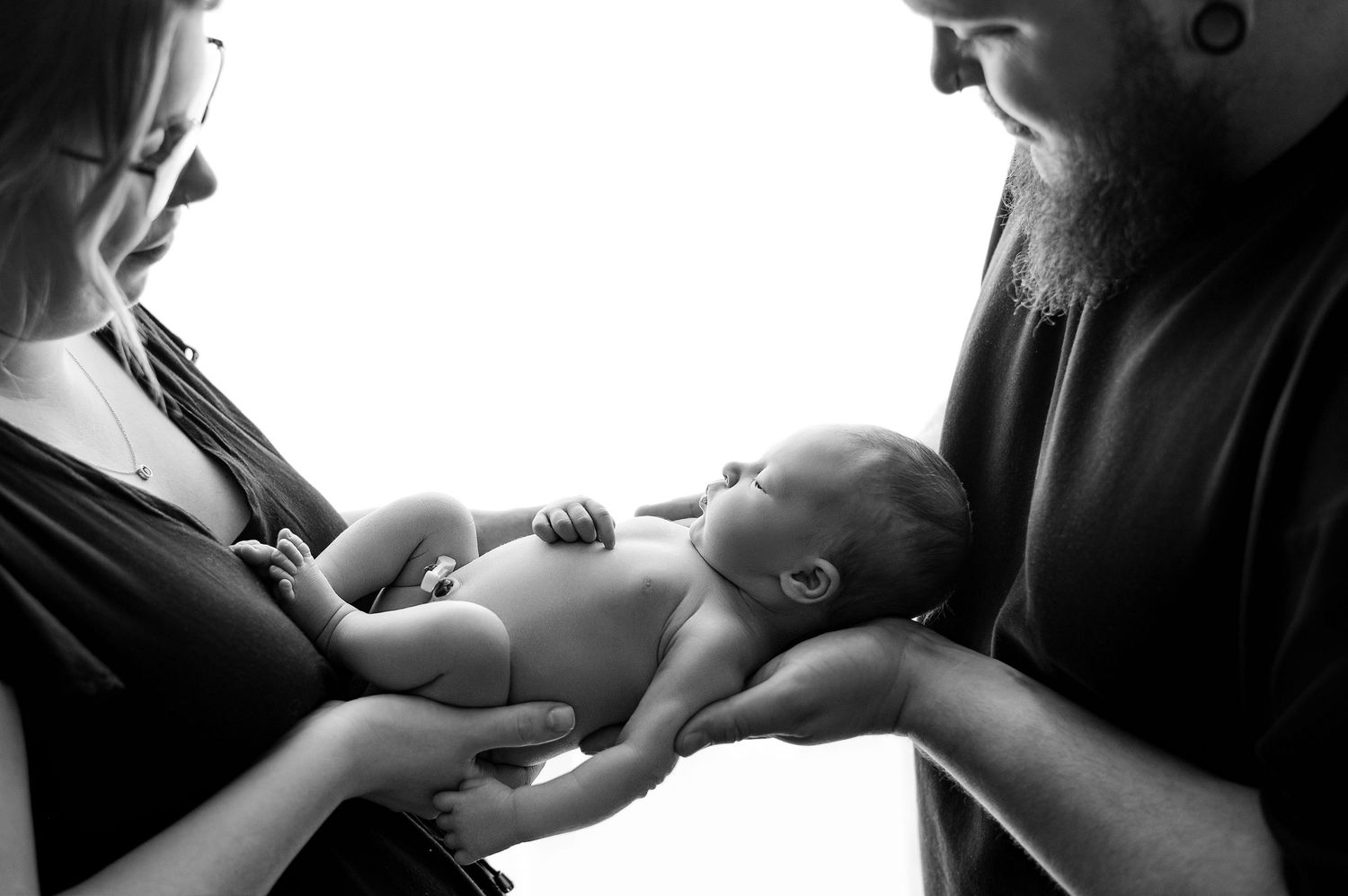 Black and white photo of parents tenderly holding their newborn baby together in a touching family portrait.