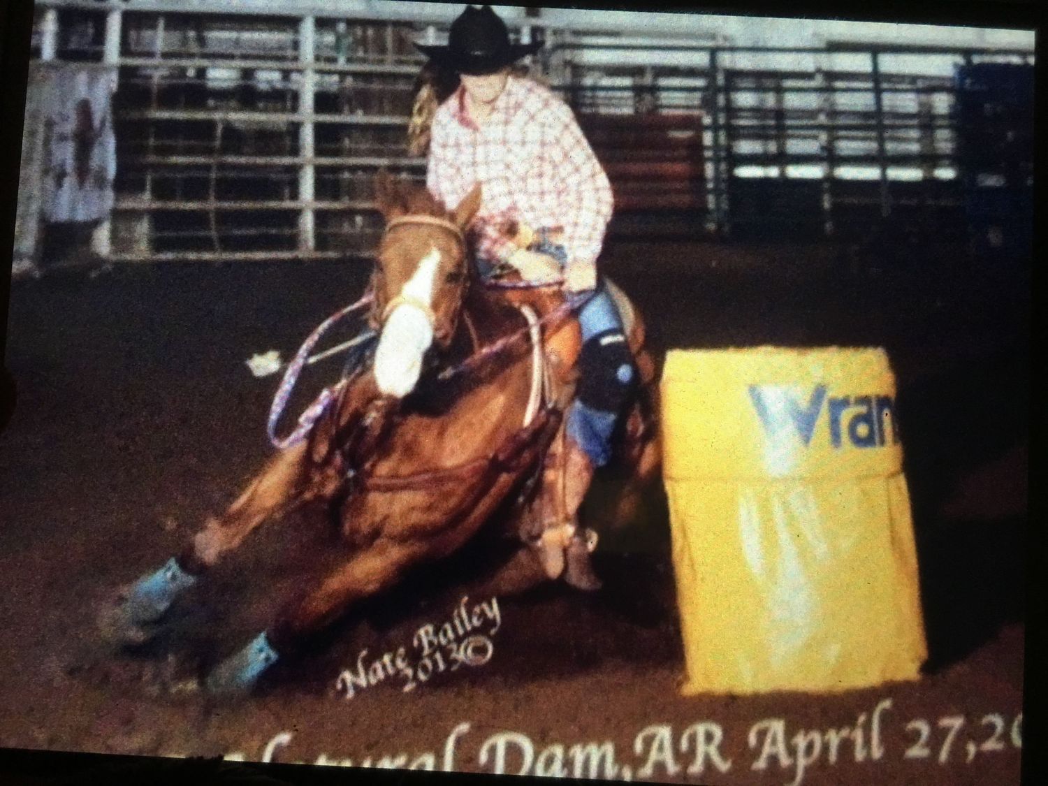 Barrel racer on horseback navigating around a yellow barrel during a rodeo competition at night.