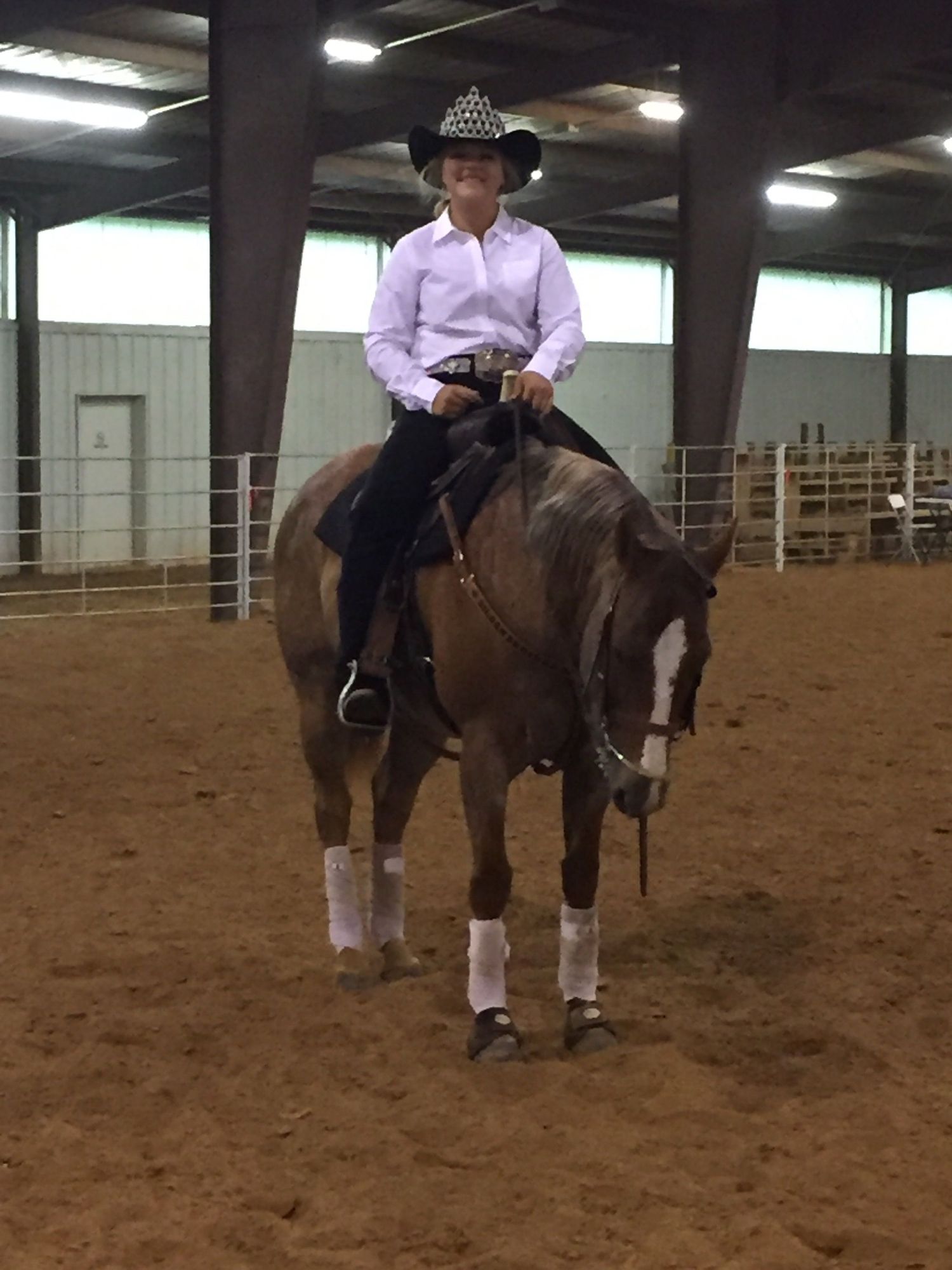 Equestrian in purple shirt and cowboy hat riding a brown horse in an indoor arena during practice.