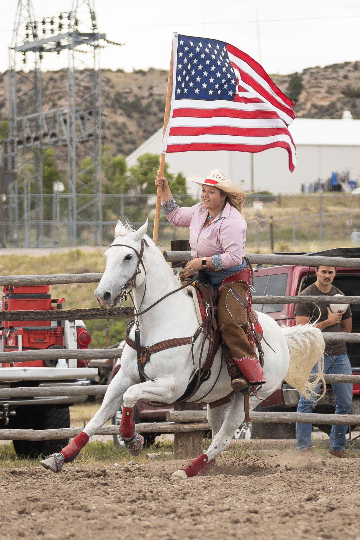 Woman on white horse carrying American flag at outdoor rodeo event.