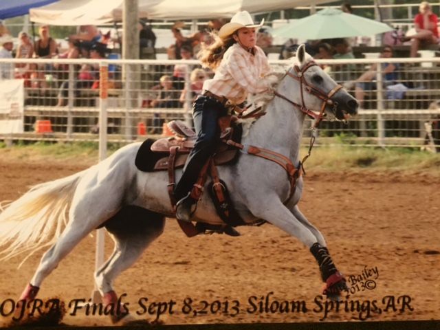 A rodeo rider on a white horse competes in barrel racing at the Siloam Springs competition in 2013.