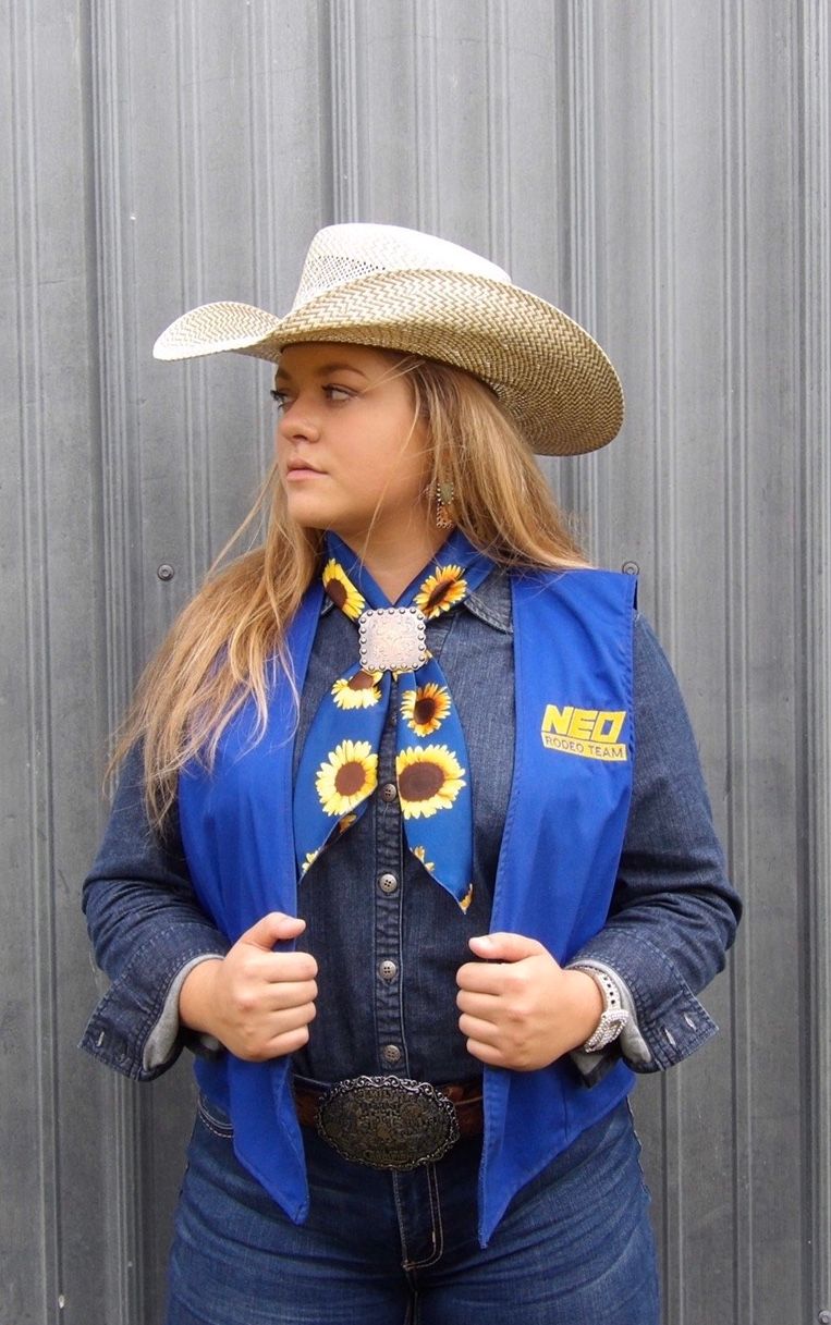 A western-styled outfit featuring a straw cowboy hat, sunflower bandana, blue NHSRA vest and denim against a gray metal wall.
