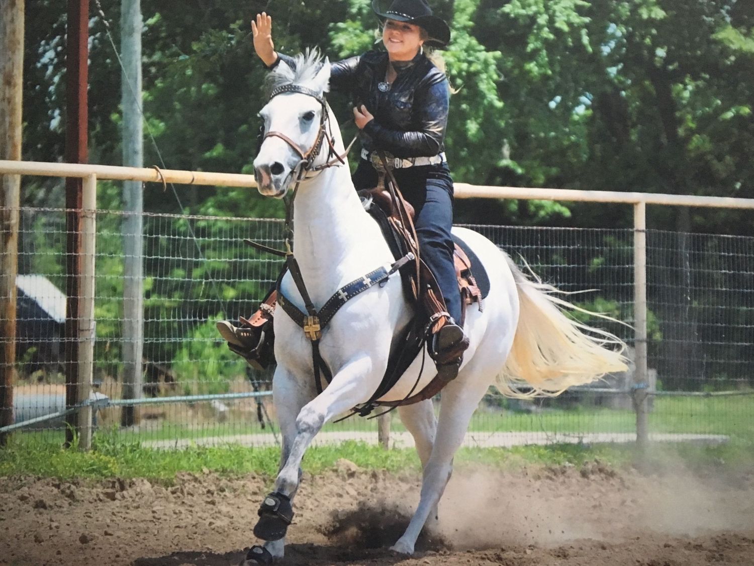 A rider in western attire guides a white horse through a dusty arena during an equestrian performance.