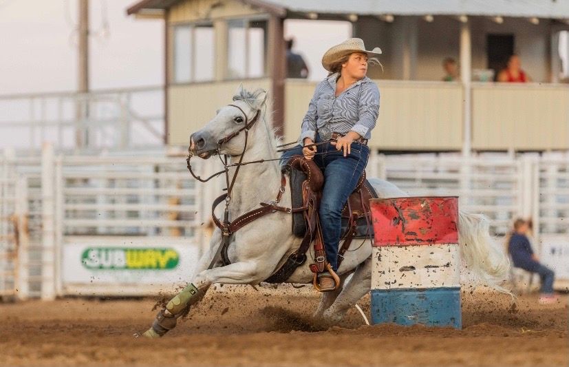 Competitive barrel racer rides a horse at high speed around an arena during a rodeo competition.