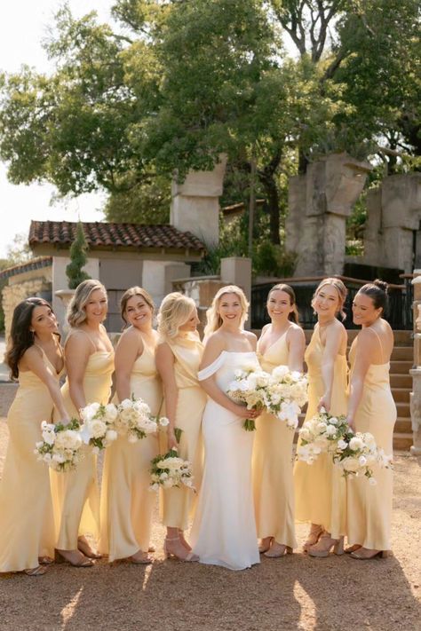 A bridal party in champagne-colored dresses poses together for a photo while holding white flower bouquets.