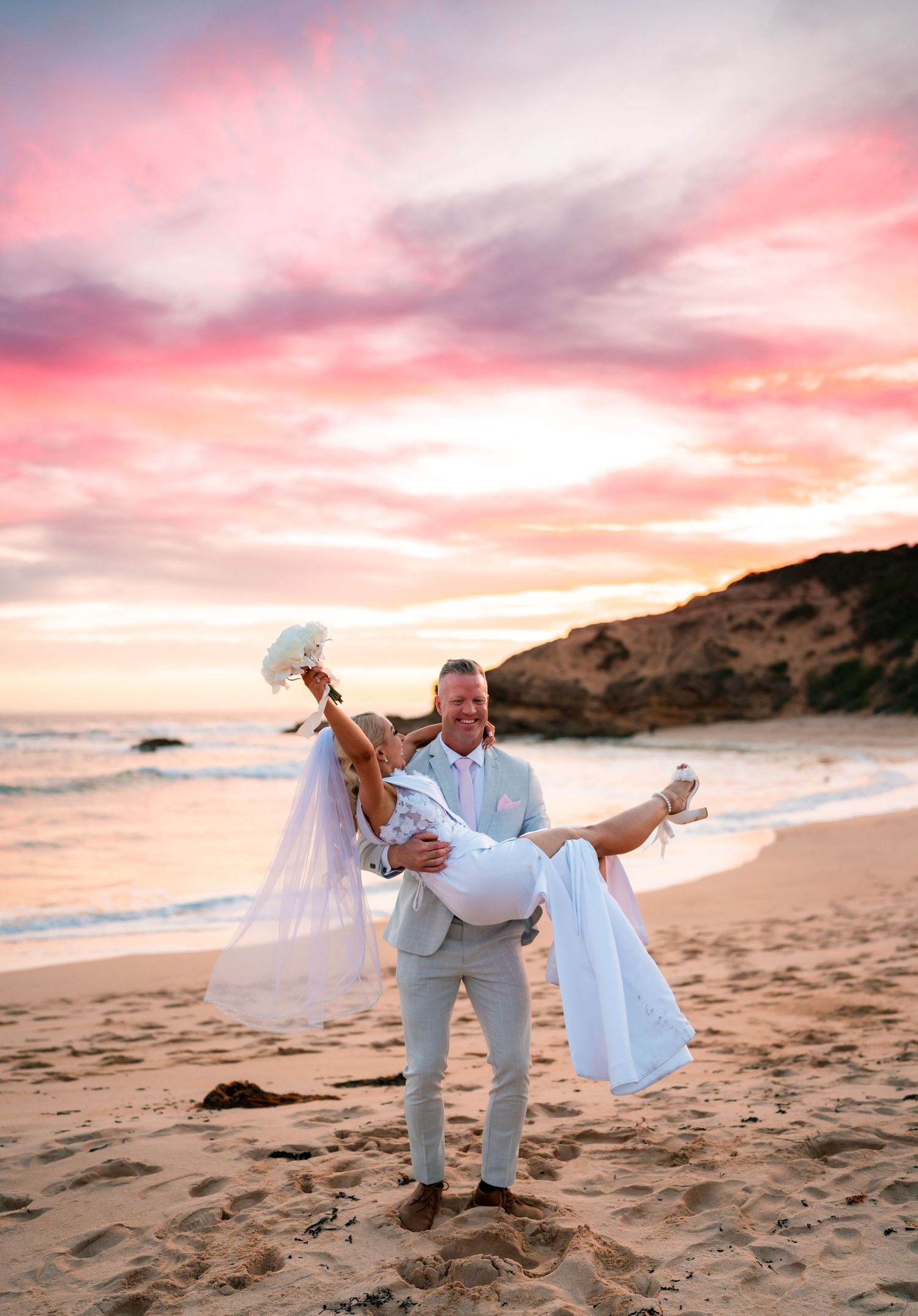 A romantic beach photoshoot at sunset with pink and purple skies over the sand and ocean.