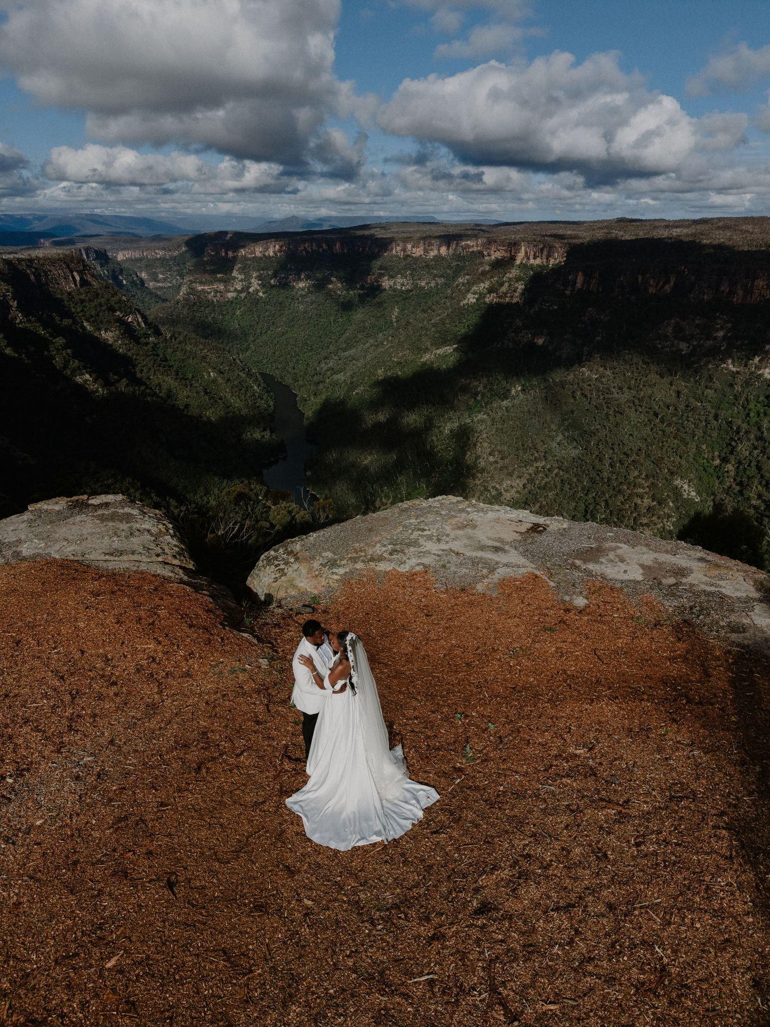 A stunning panoramic sequence of a person in white dress sitting on red rocks overlooking a vast canyon landscape.