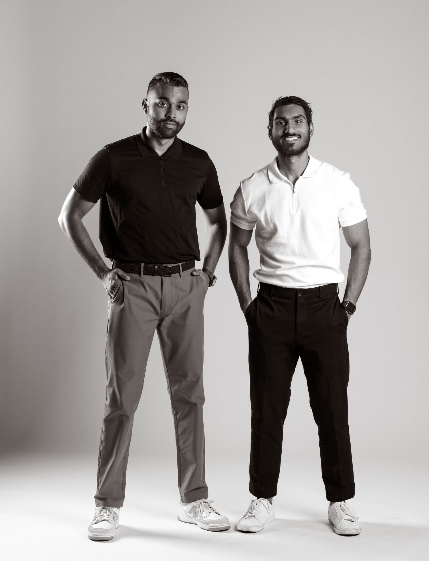 Two men stand side by side wearing casual attire in a black and white studio portrait.