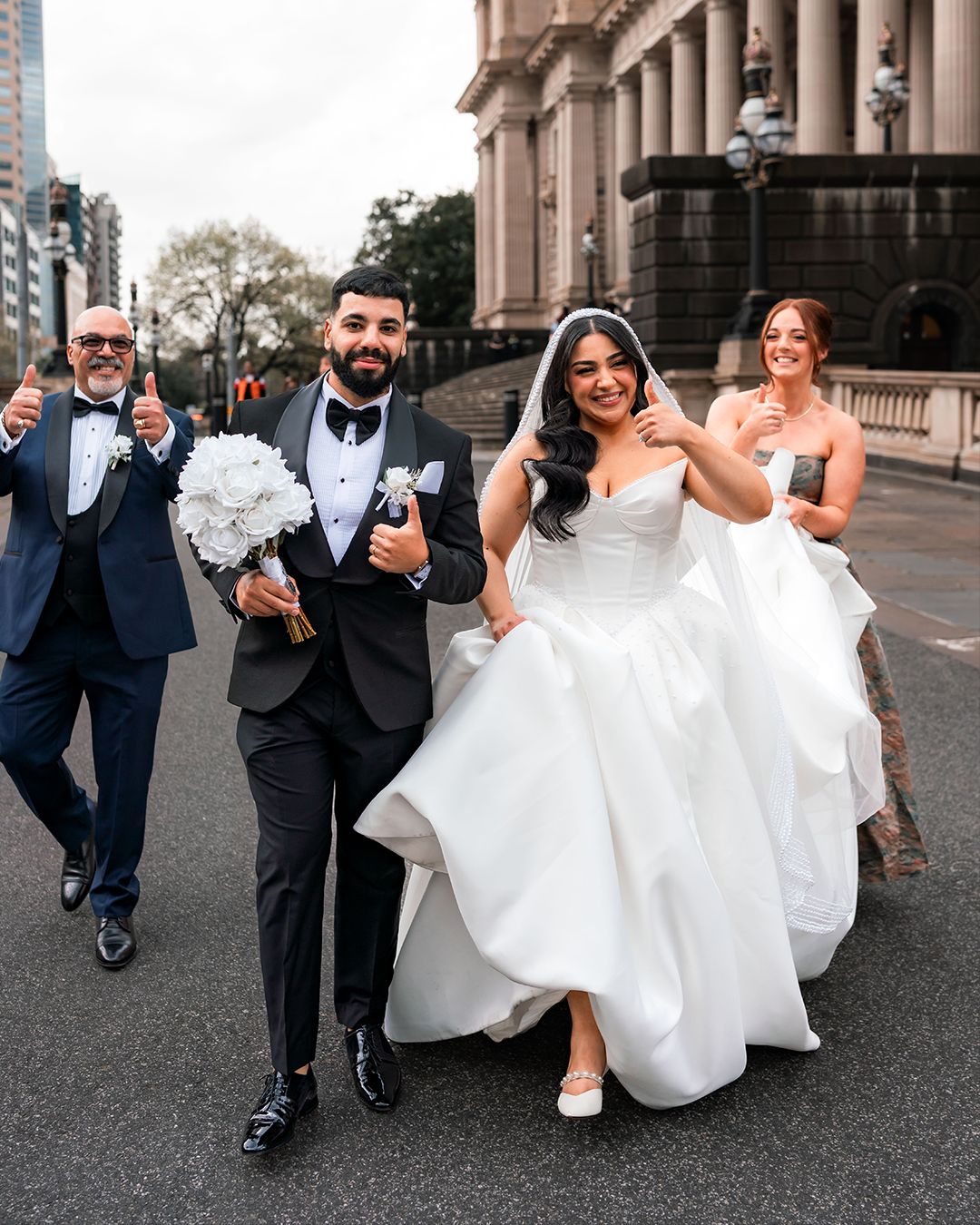Wedding party walking and laughing together outside a grand building with classical architecture.