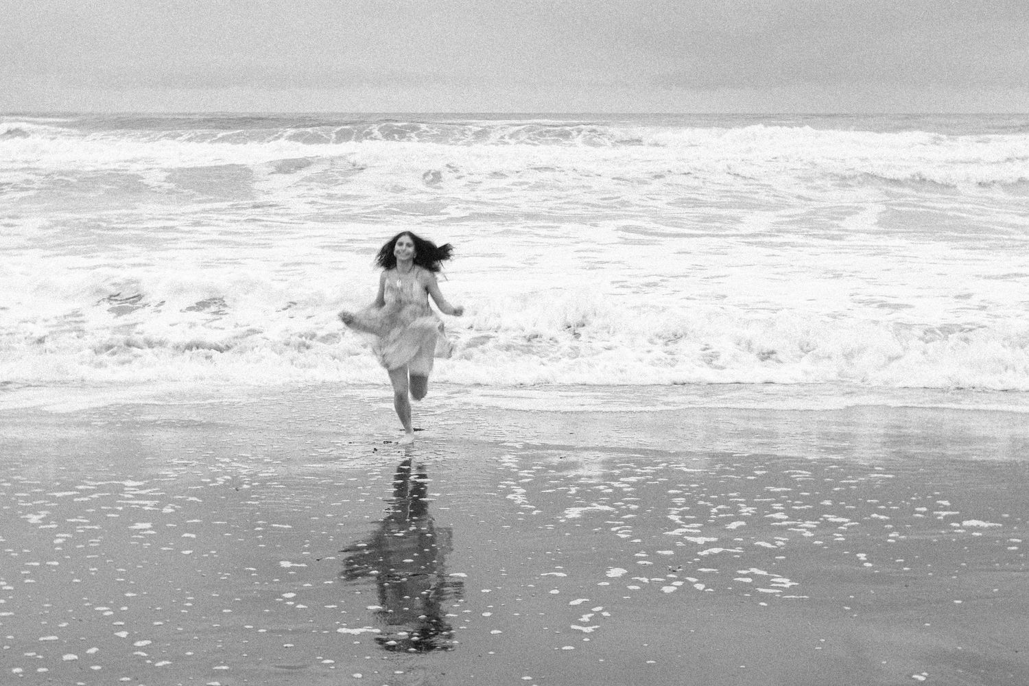 Black and white portrait of a high school senior walking along the ocean shoreline.