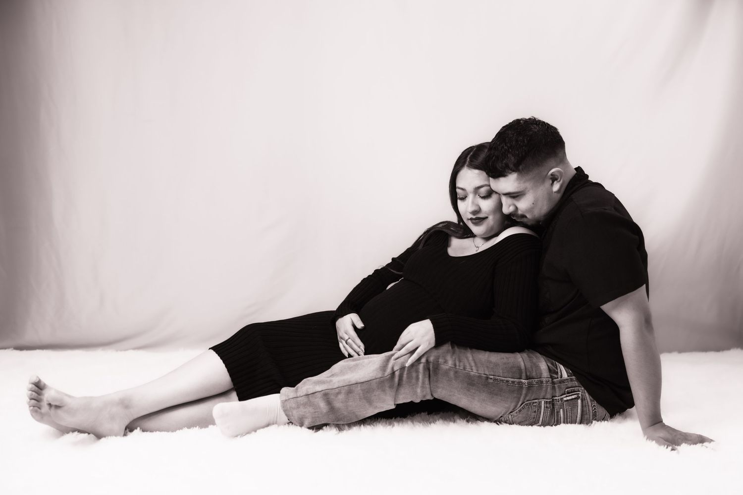Expectant parents sit closely together during an intimate black-and-white maternity session.