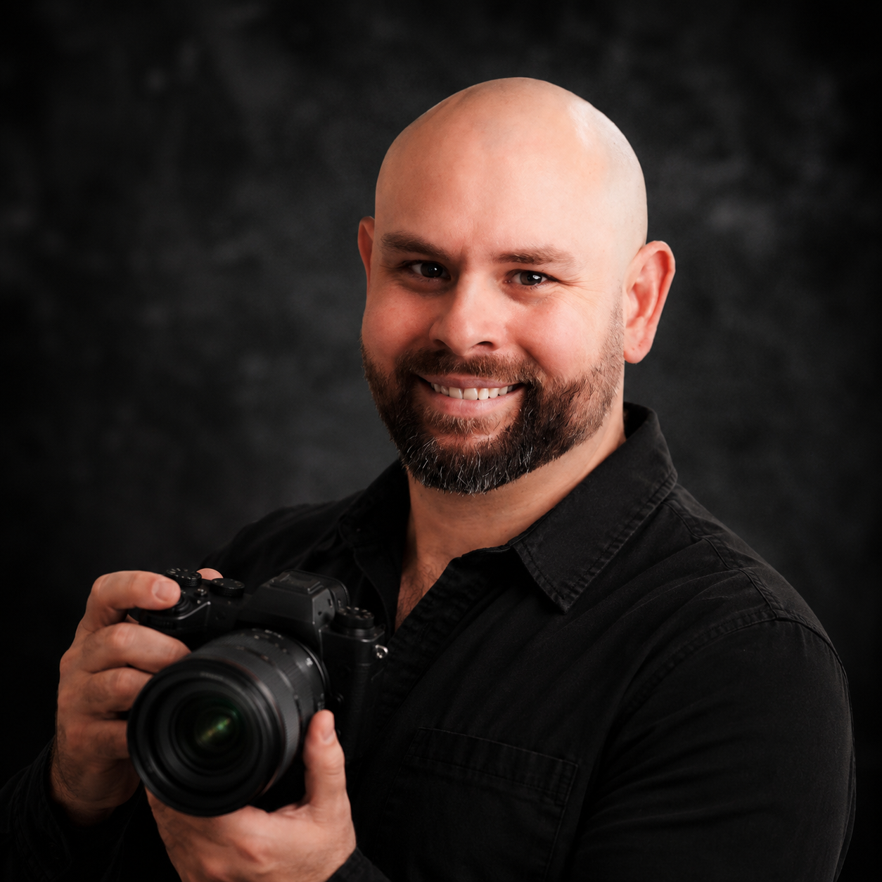 Professional studio headshot of a photographer holding a camera against a dark background.