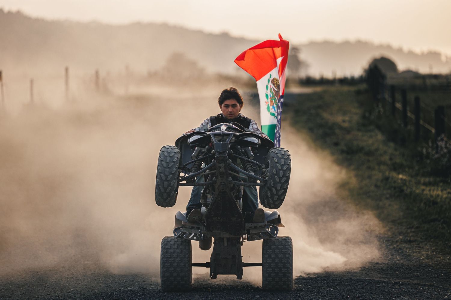 High school senior riding an ATV along a dusty rural trail during an outdoor senior portrait session.