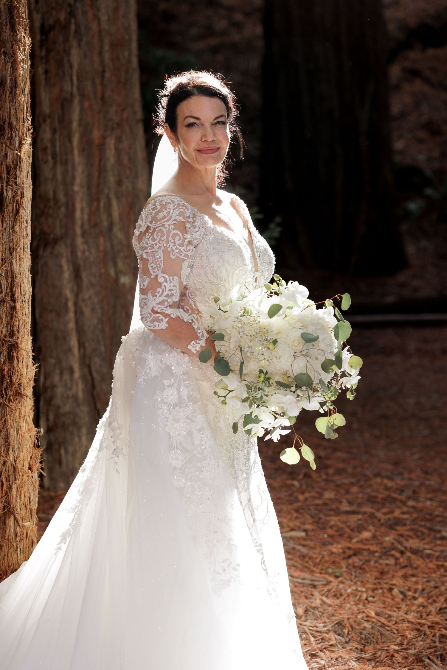 Bride holding a bouquet among the redwood trees on her wedding day.