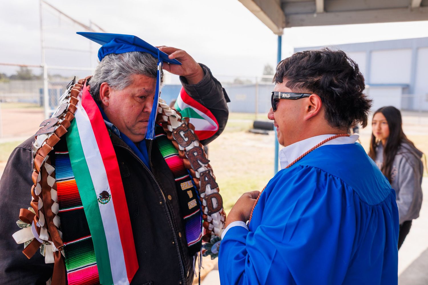 Graduate in a blue cap and gown receives a colorful ceremonial stole after graduation.