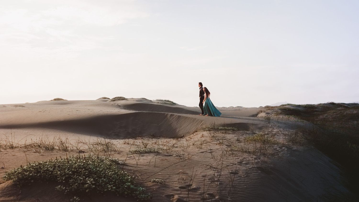 Couple sitting together among coastal sand dunes during an intimate outdoor engagement photography session.