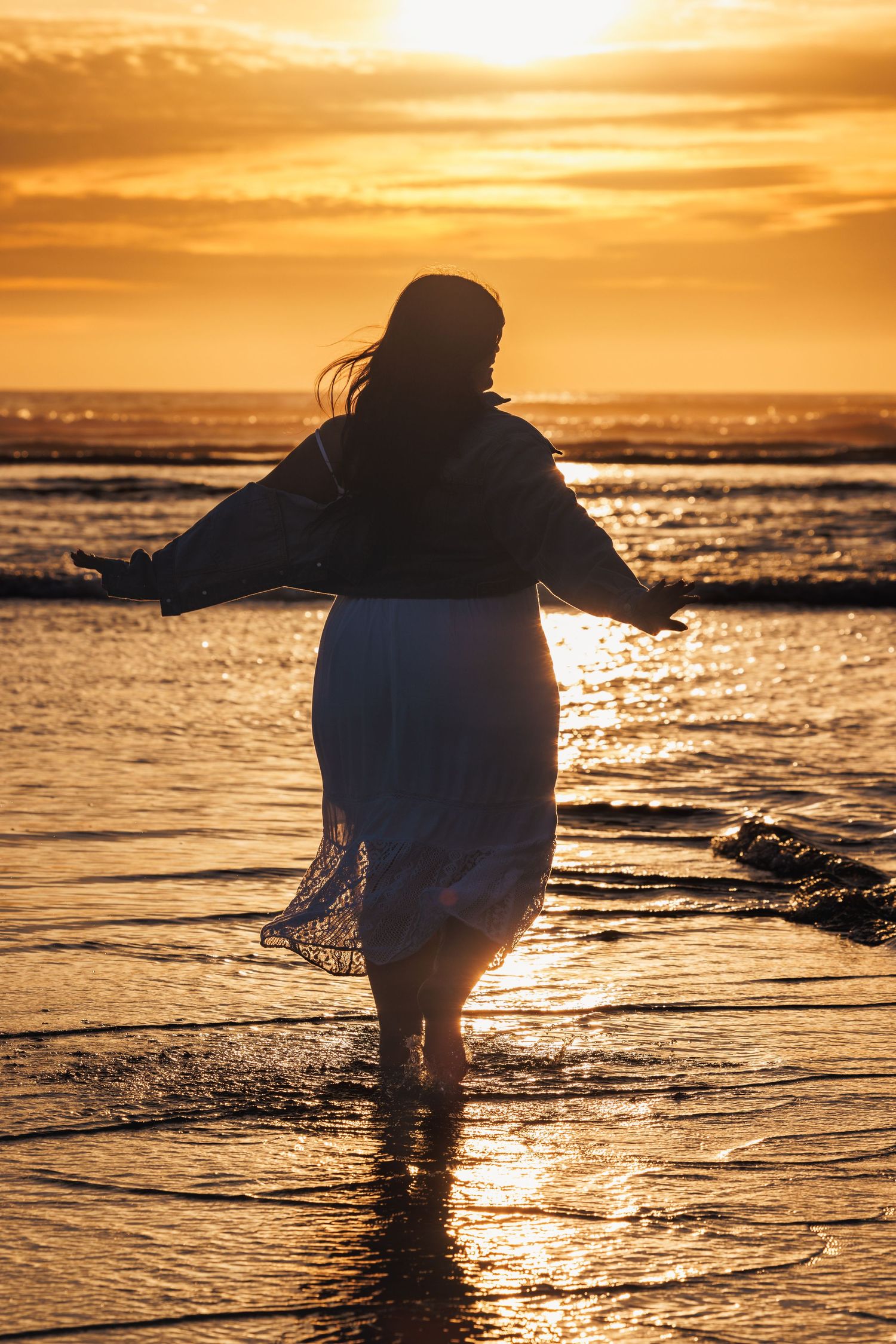 High school senior standing along the shoreline at sunset during a golden-hour beach portrait session.