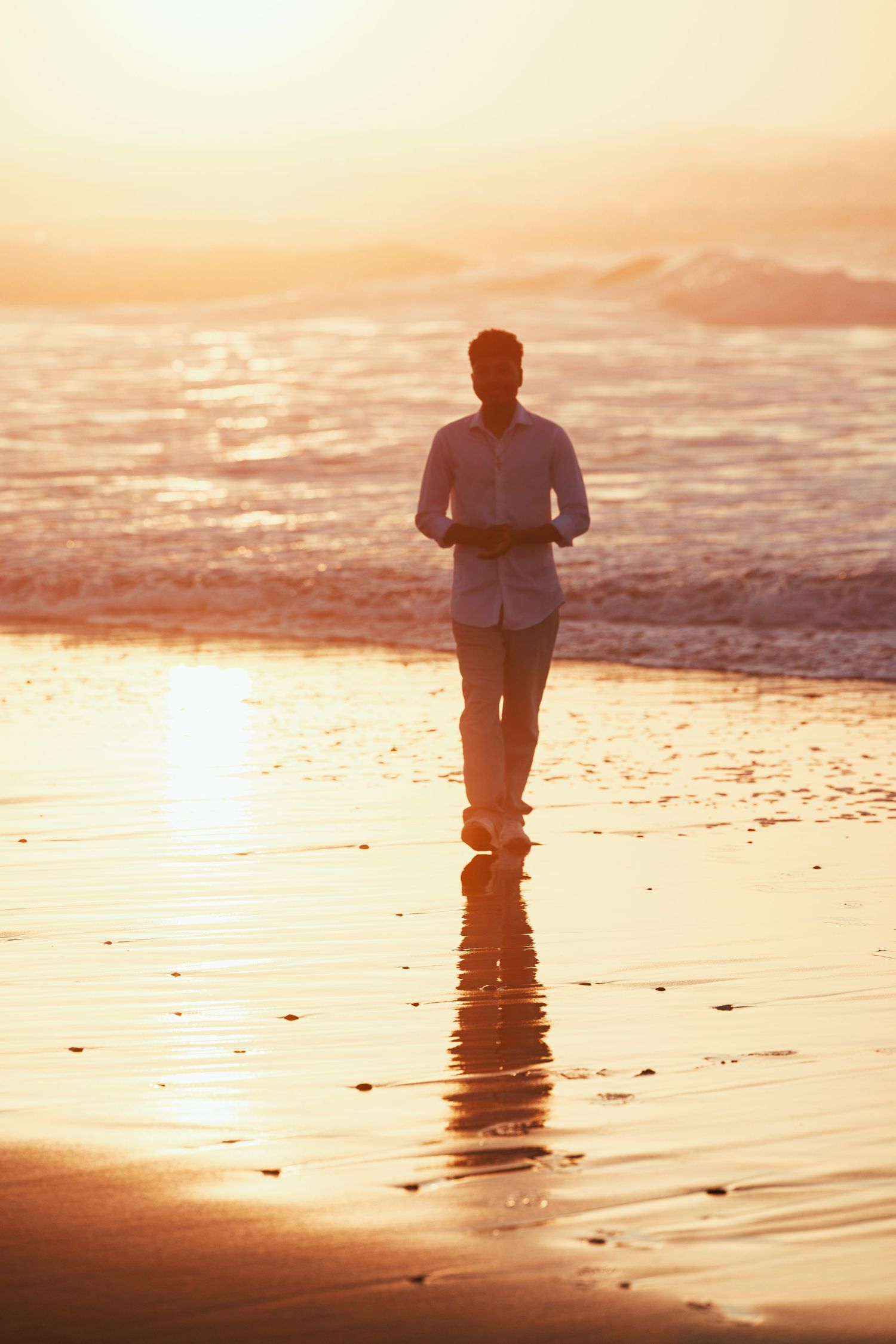 High school senior standing on a reflective beach shoreline during a warm sunset portrait session.
