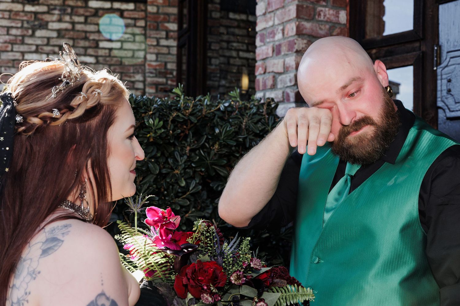 Emotional groom wipes away tears while looking at his bride during their outdoor wedding ceremony.