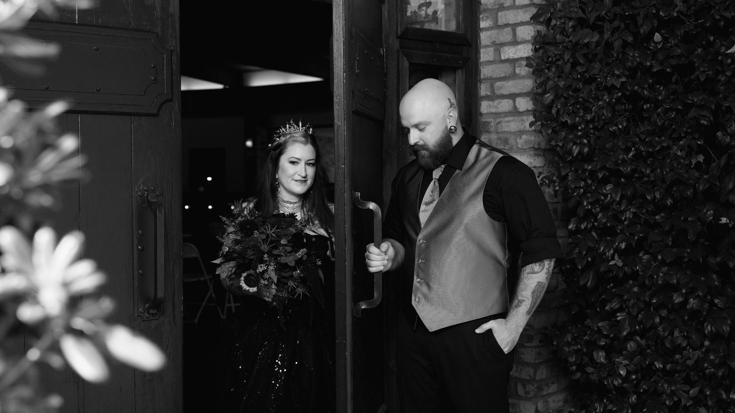 Bride and groom walk together through a doorway in a candid black-and-white wedding portrait.