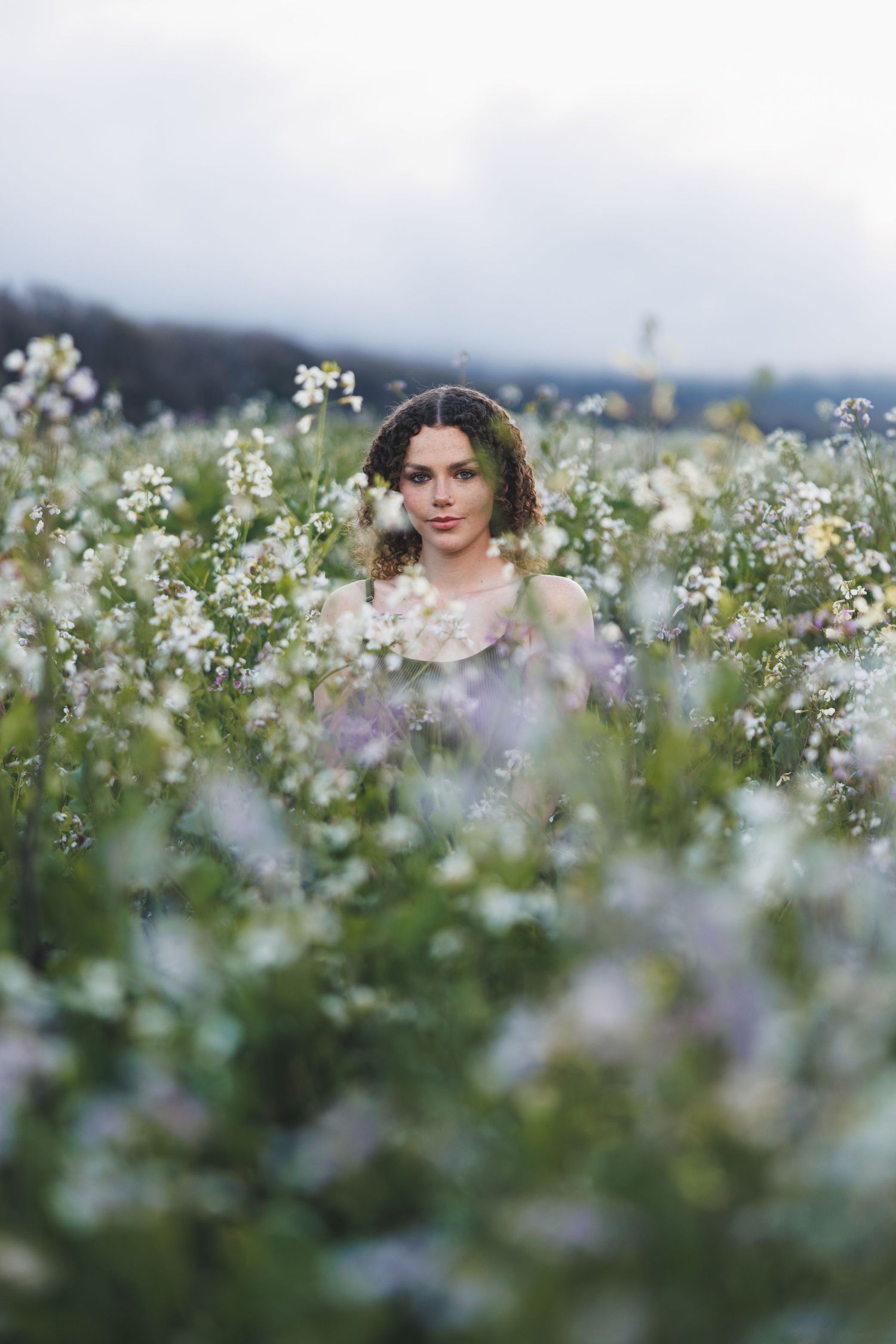 High school senior standing among white wildflowers during an outdoor portrait session with soft natural light.