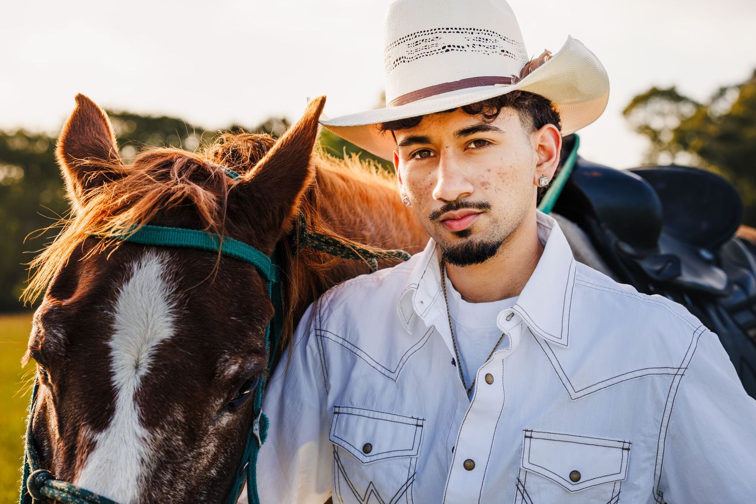 High school senior wearing a cowboy hat posing beside a horse during a western senior portrait session.