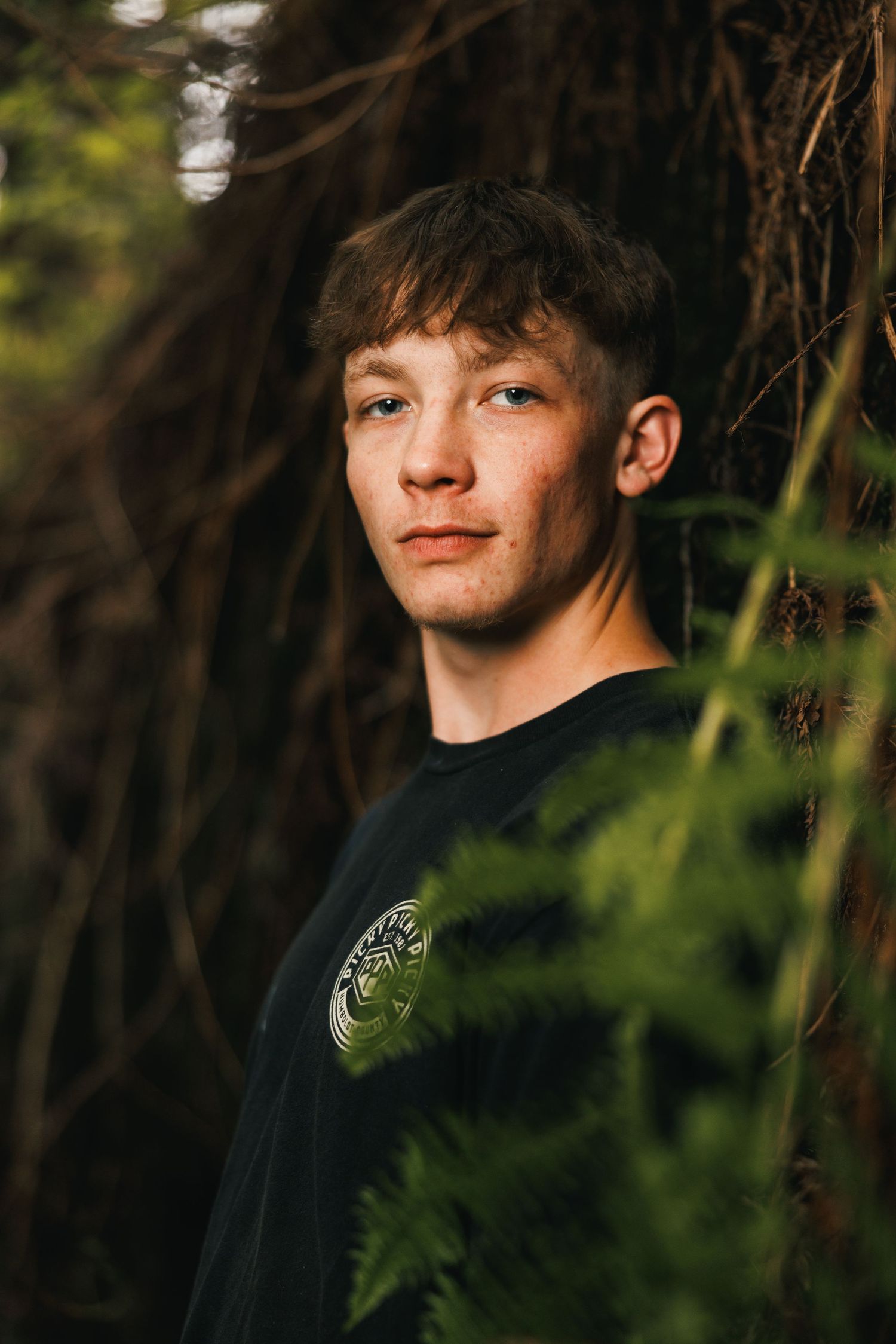 High school senior posing among green foliage during an outdoor portrait session with soft natural light.