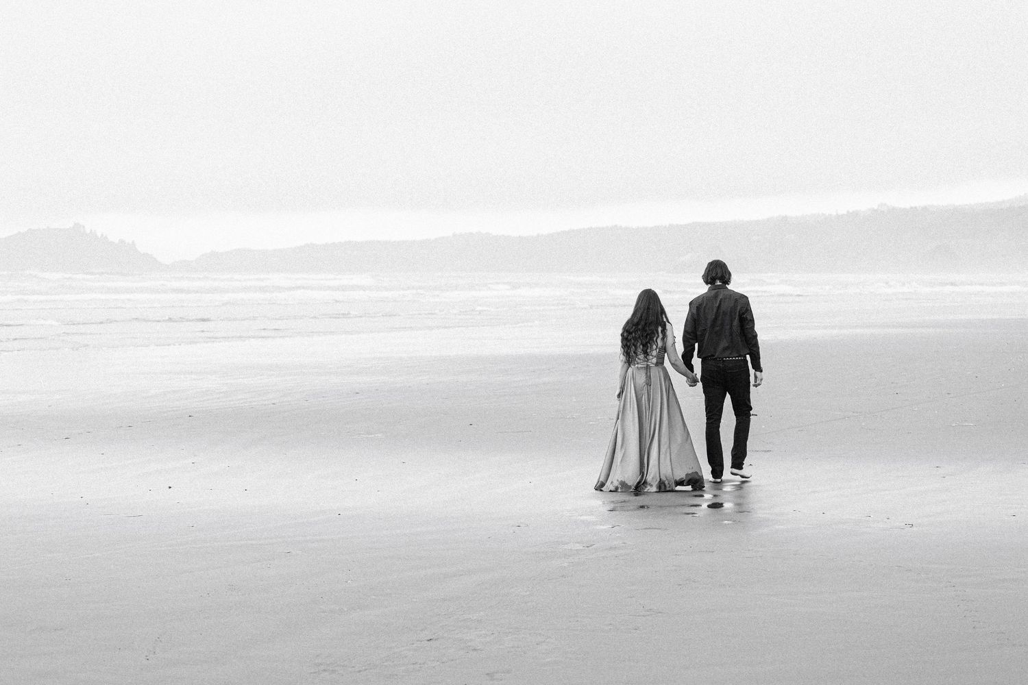 Couple stands together on an expansive beach in a black-and-white portrait.