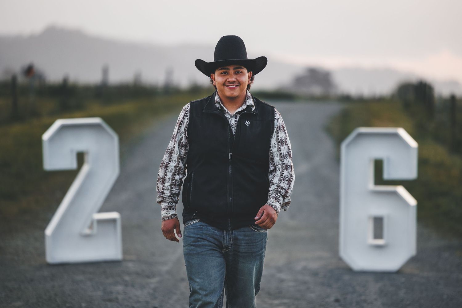High school senior wearing a cowboy hat and western attire posing with large 2026 graduation numbers outdoors.