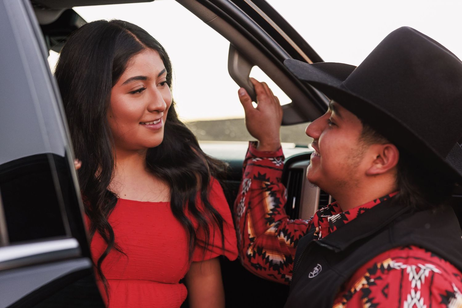 Cowboy gently brushes his partner’s hair beside a vehicle during a couples session.