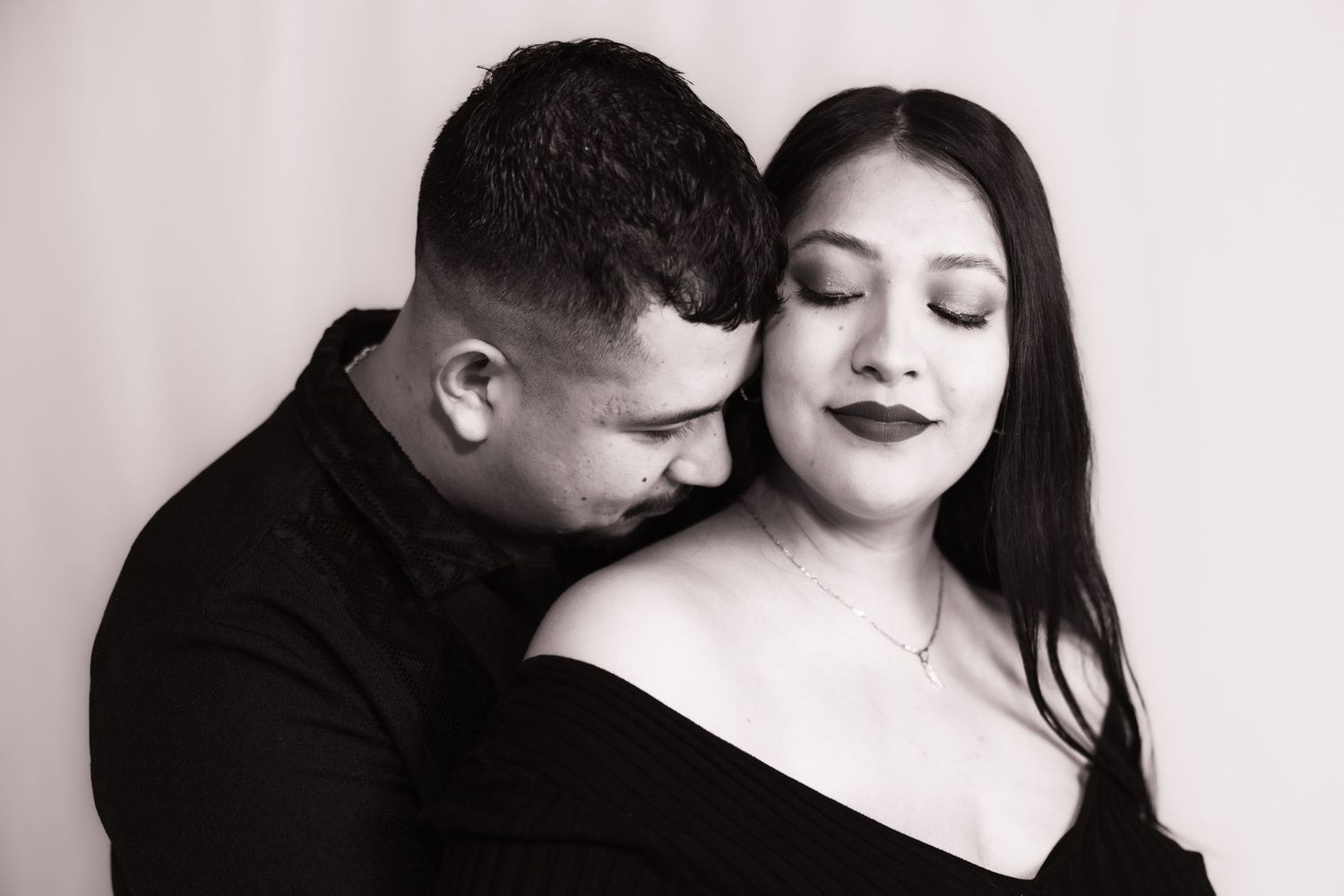 Expectant father embraces his partner from behind during a black-and-white maternity portrait.