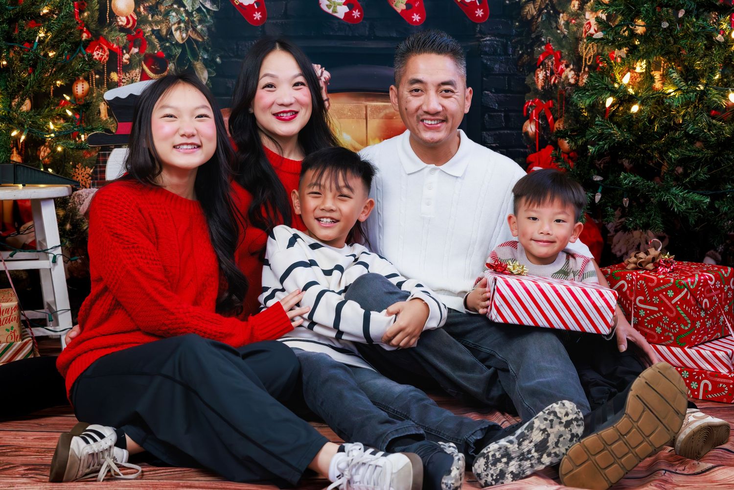 Family of five sitting together for a Christmas portrait with festive holiday decorations and red accents.