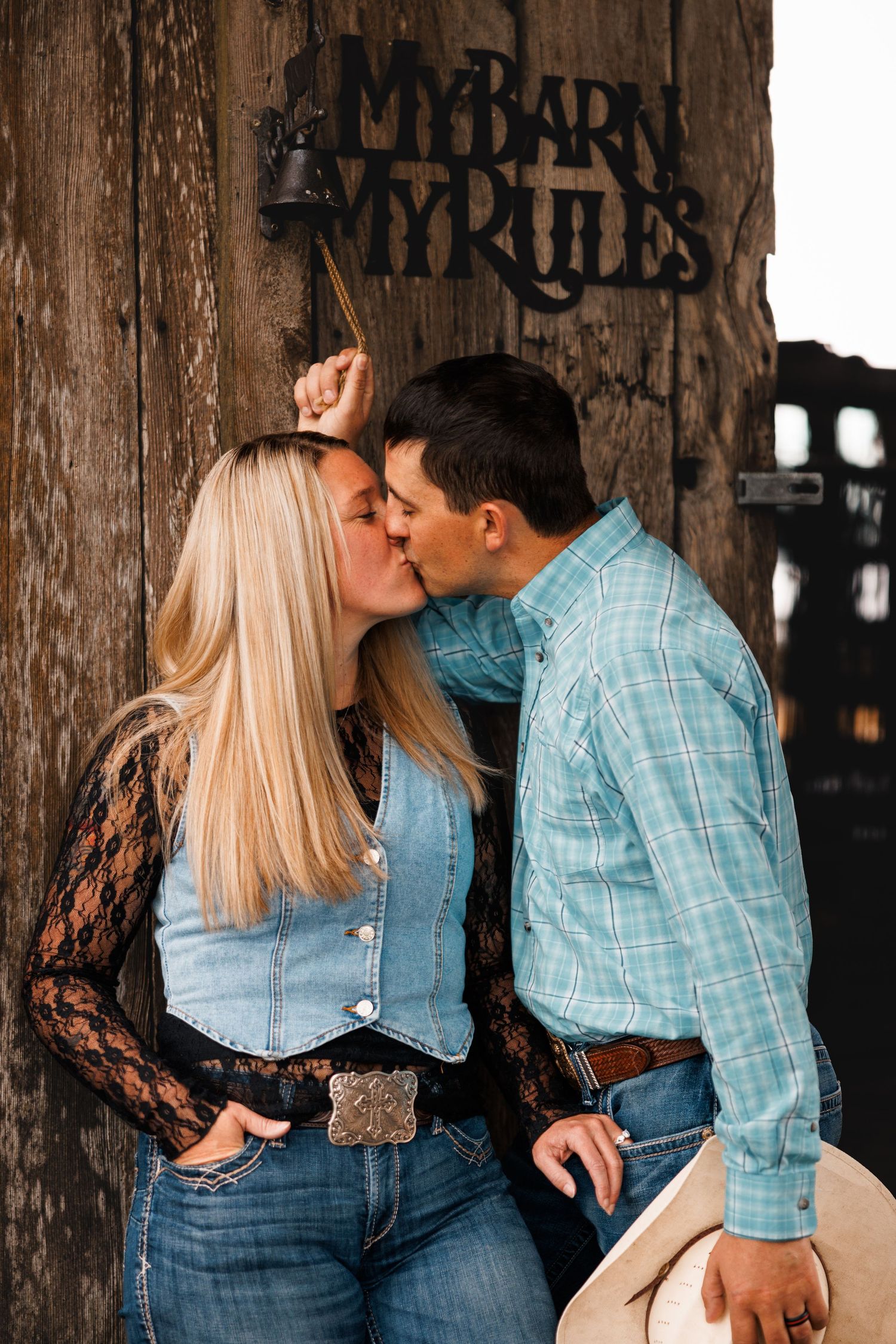 Couple kisses beside a rustic wooden barn during a country engagement session.
