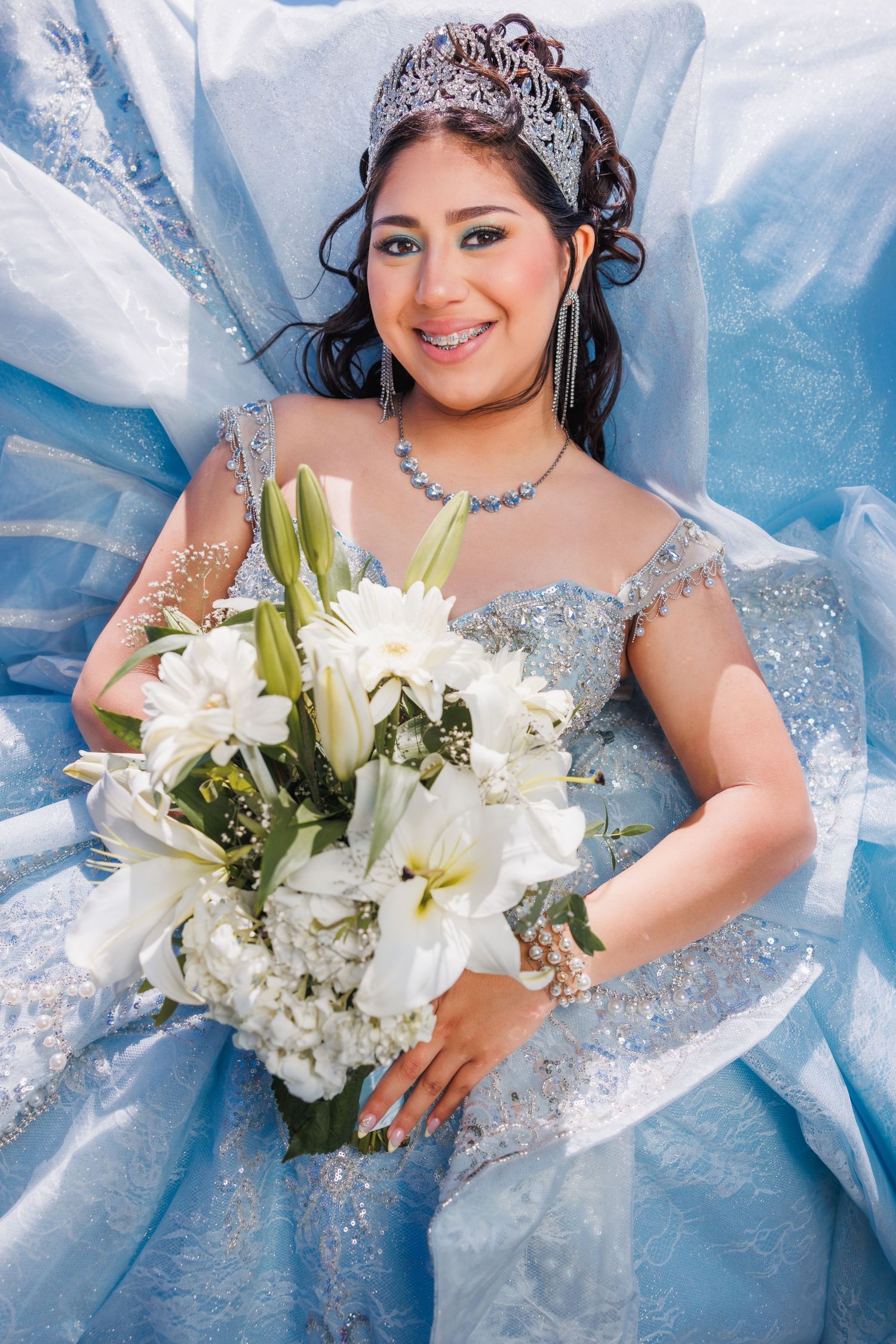 Quinceañera poses in a blue gown while holding a bouquet of white flowers.