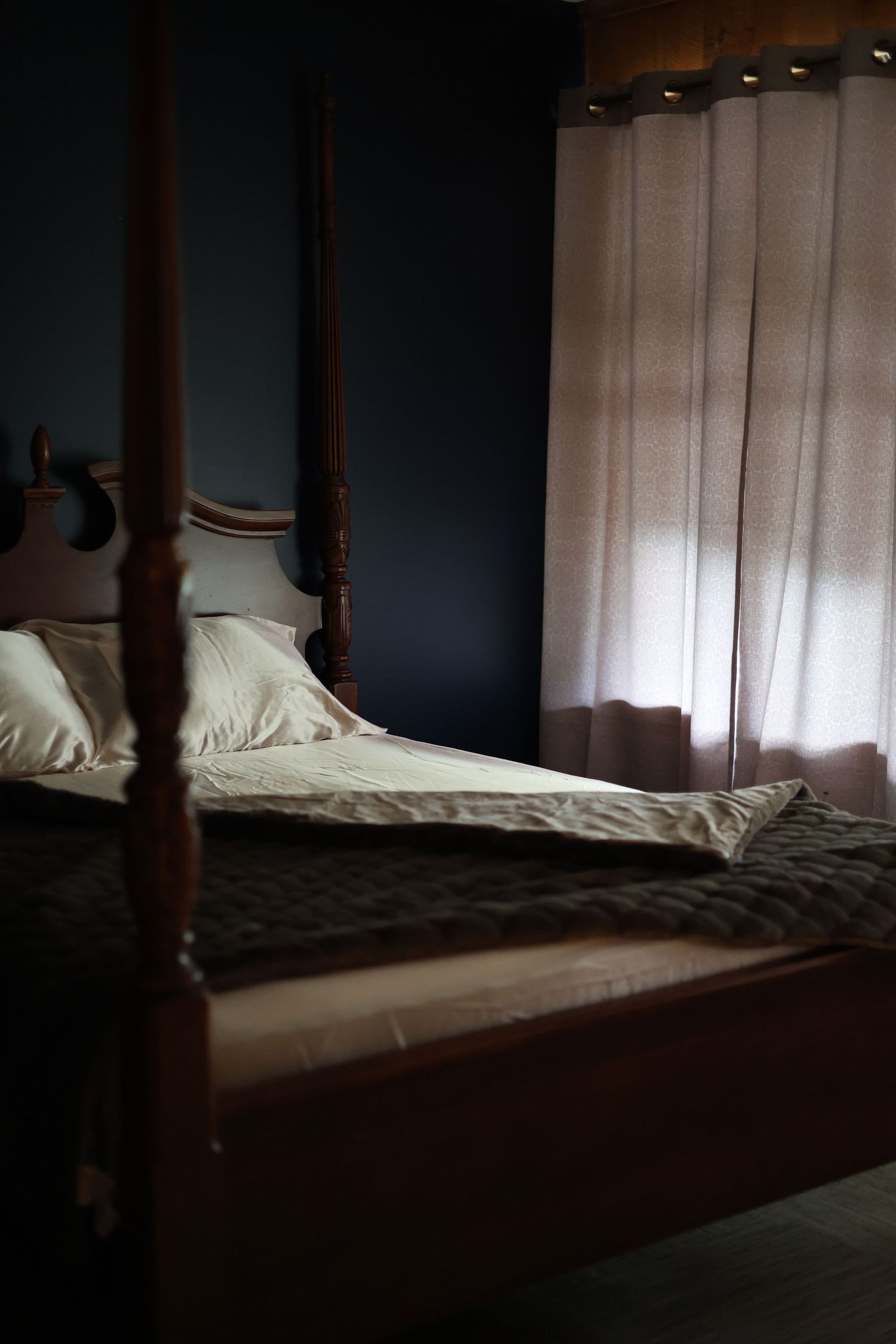 Four poster bed with soft linens beside a curtained window in the moody Savory Room boudoir studio.