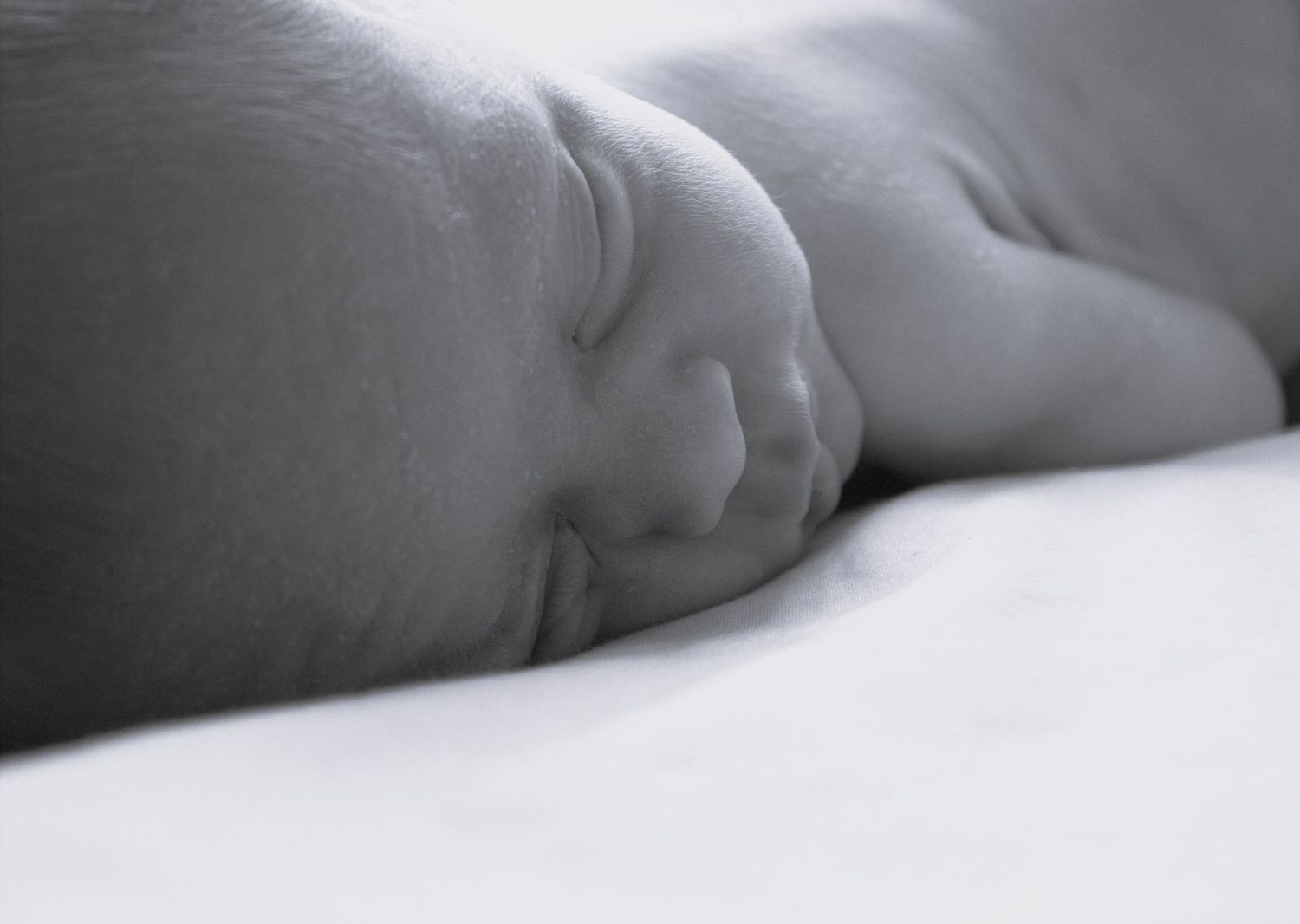 Peaceful newborn baby sleeping face down on white surface in soft black and white photo.