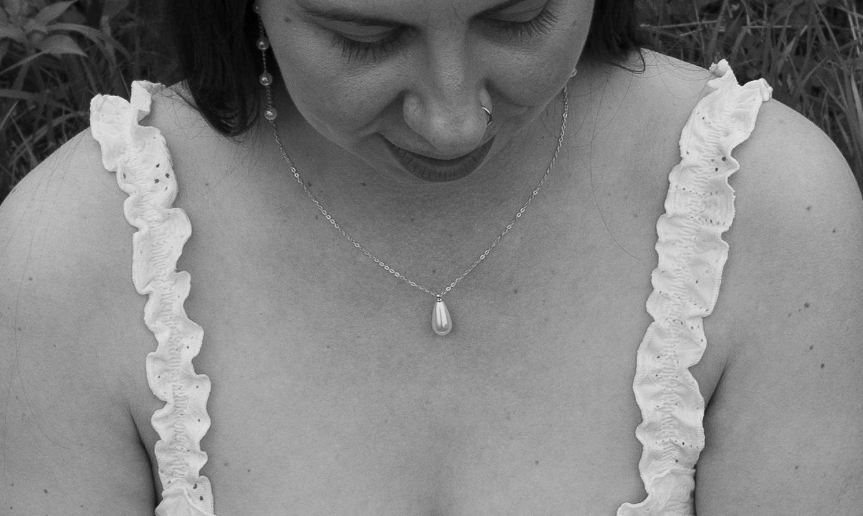Black and white close-up of a woman in a white ruffled dress wearing a delicate teardrop necklace.