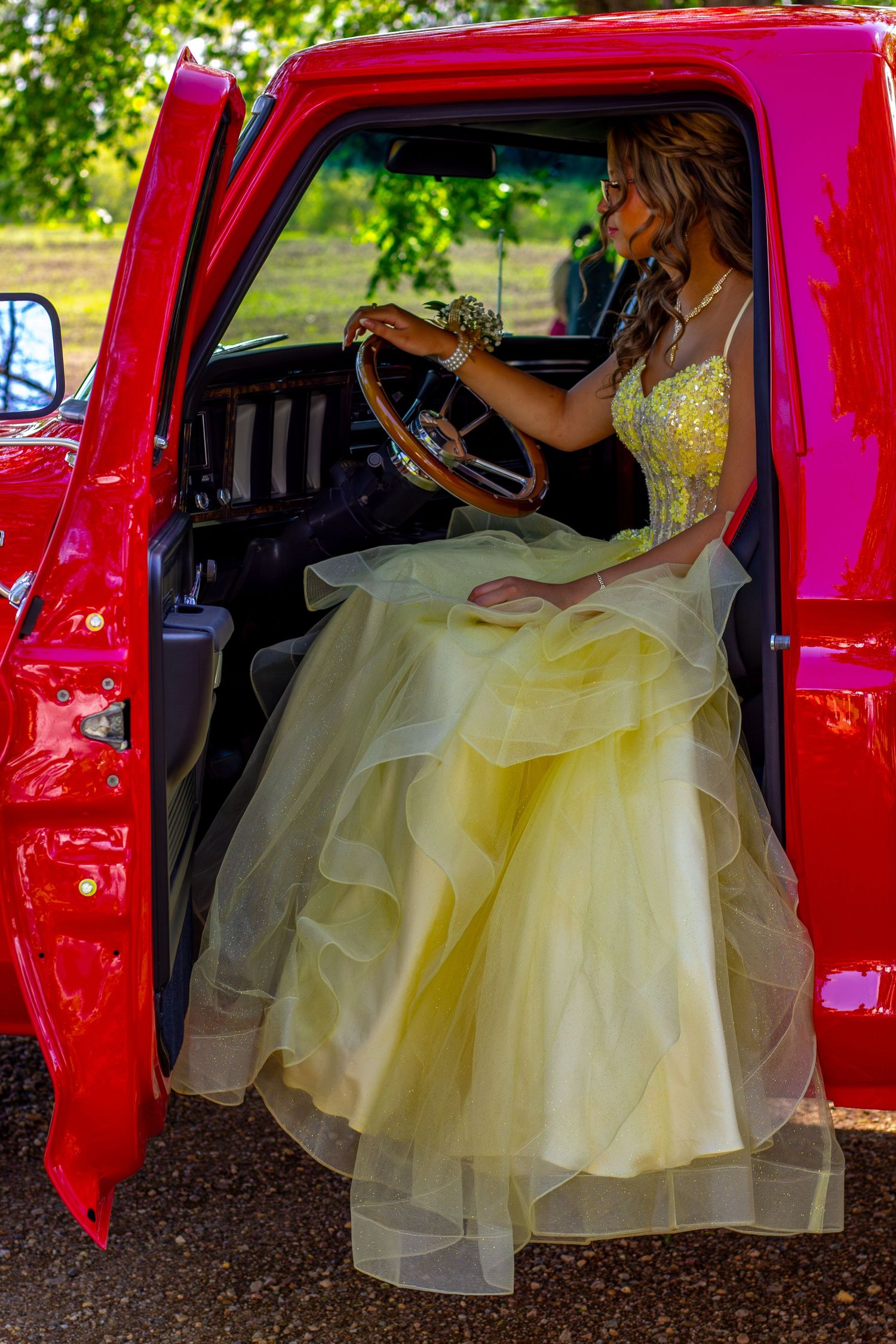 Young woman in elegant yellow ball gown sitting in the open door of a classic red pickup truck.