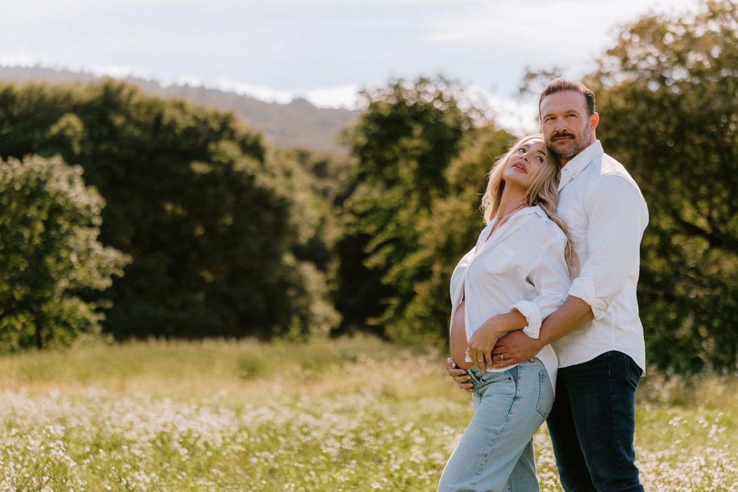 Expecting couple embracing in a sunlit field during a maternity photography session at Filoli Gardens.