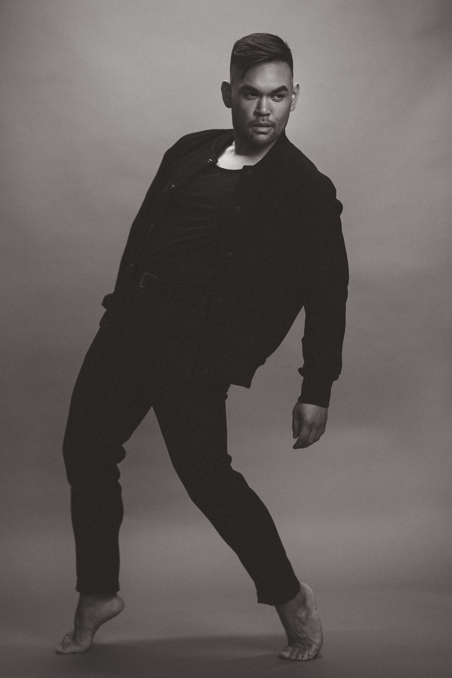 Black and white portrait of photographer RyanVincent Alvarez in a dance-inspired pose against a studio backdrop.