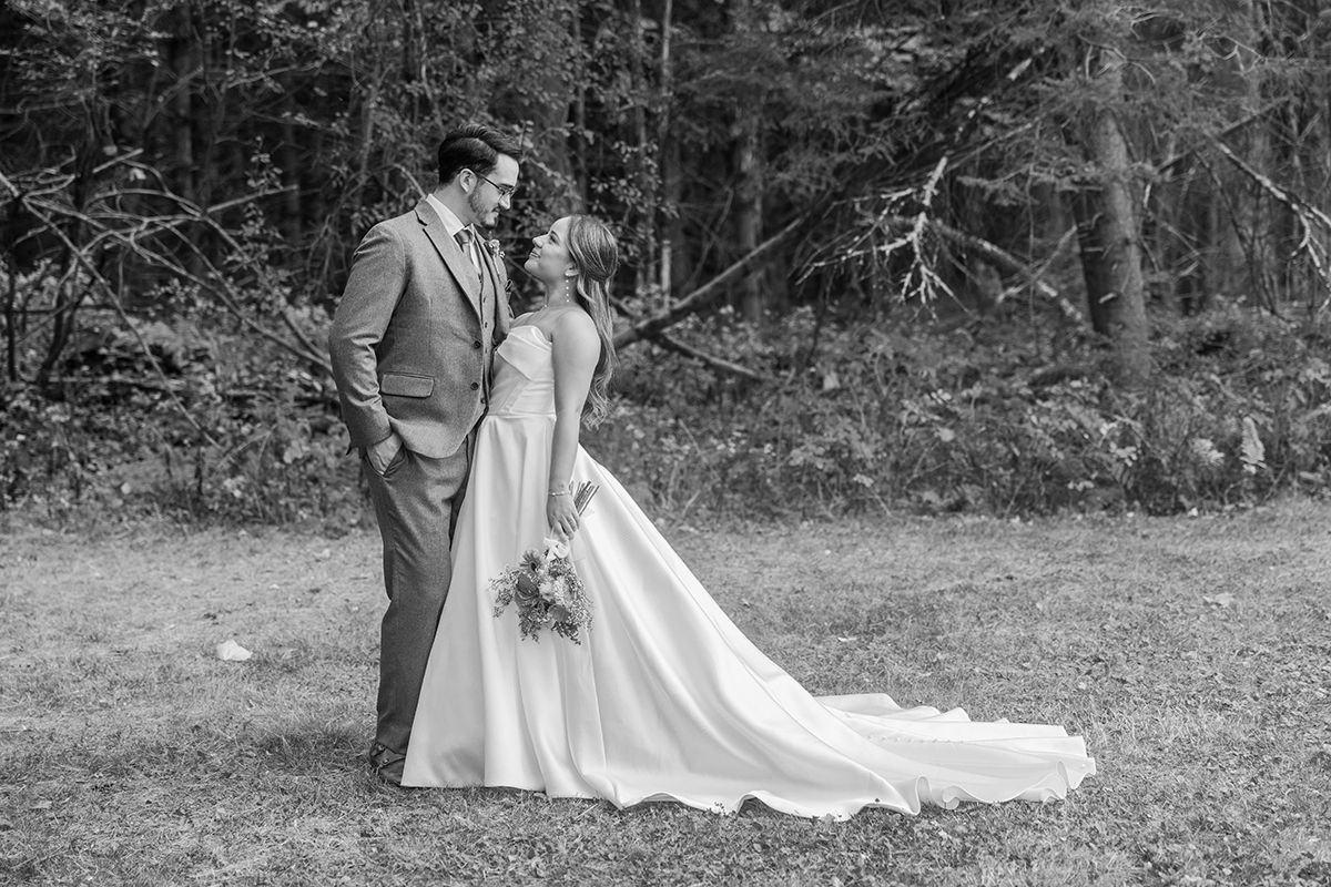 A bride and groom share a romantic black and white portrait moment in a wooded outdoor setting.