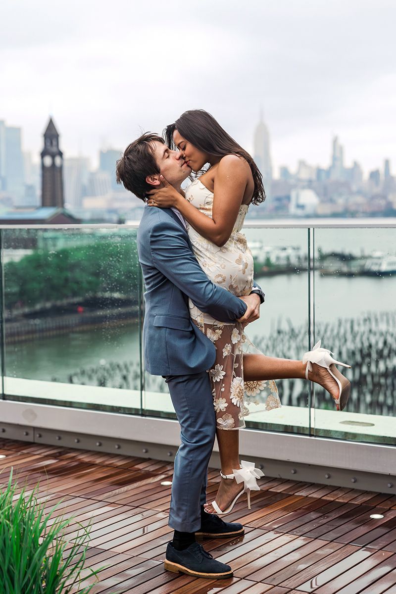 Couple sharing a romantic kiss on a rooftop terrace with the New York City skyline in the background.