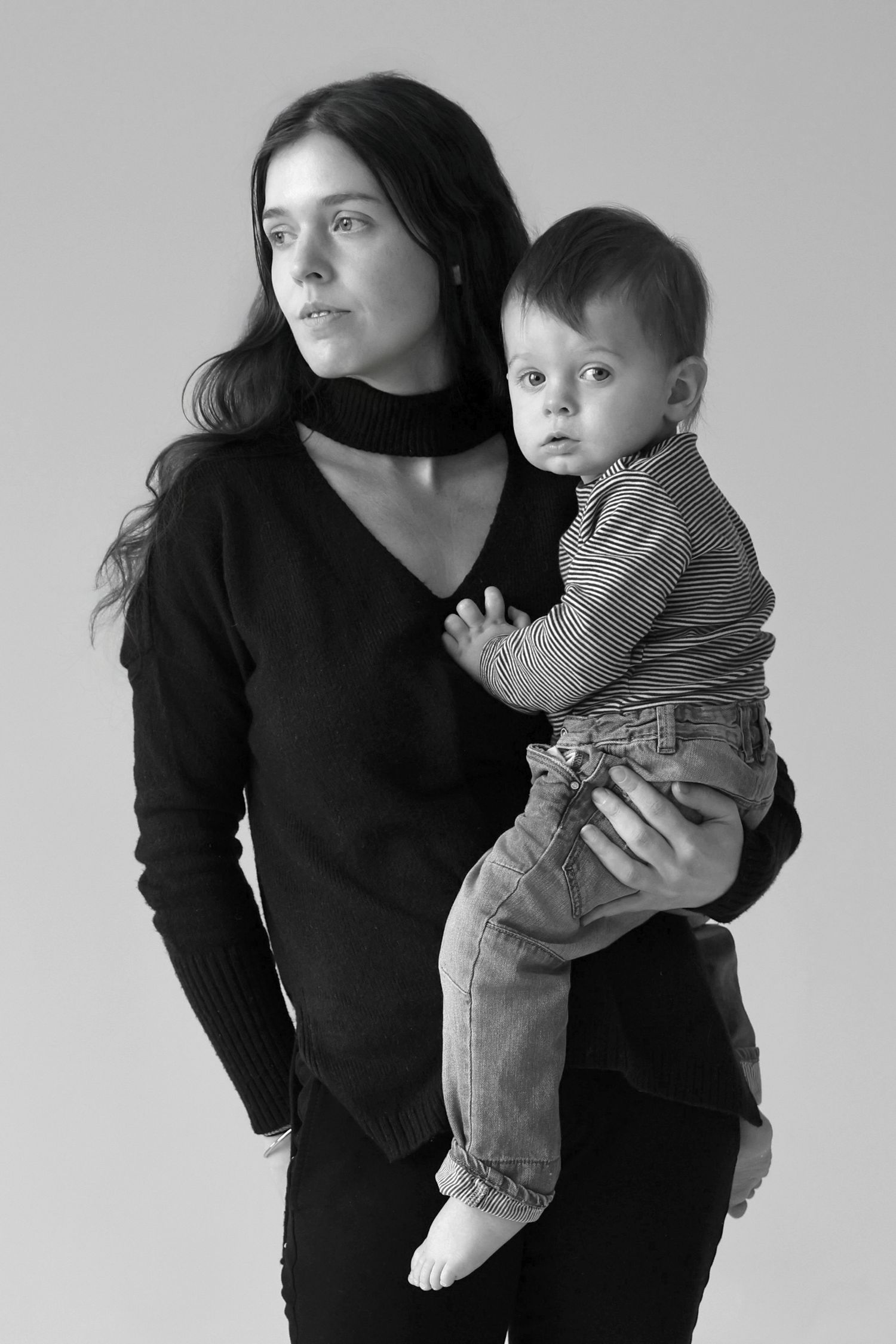 Black and white photo of dark-haired woman holding young baby in striped outfit.