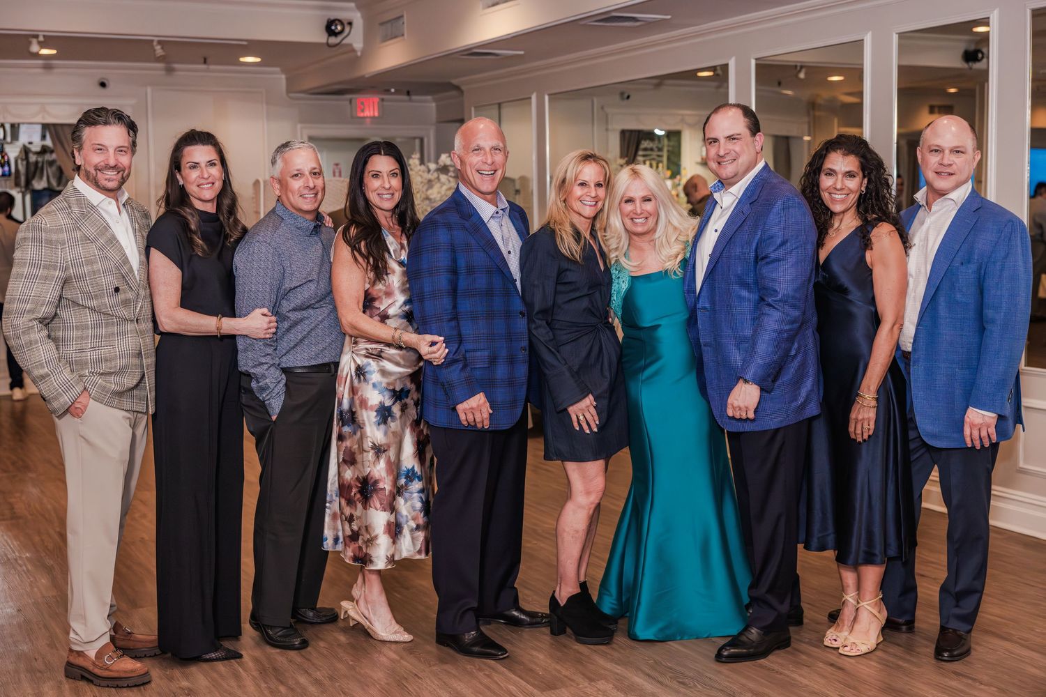 Group of elegantly dressed adults posing together at a formal event in a bright venue.