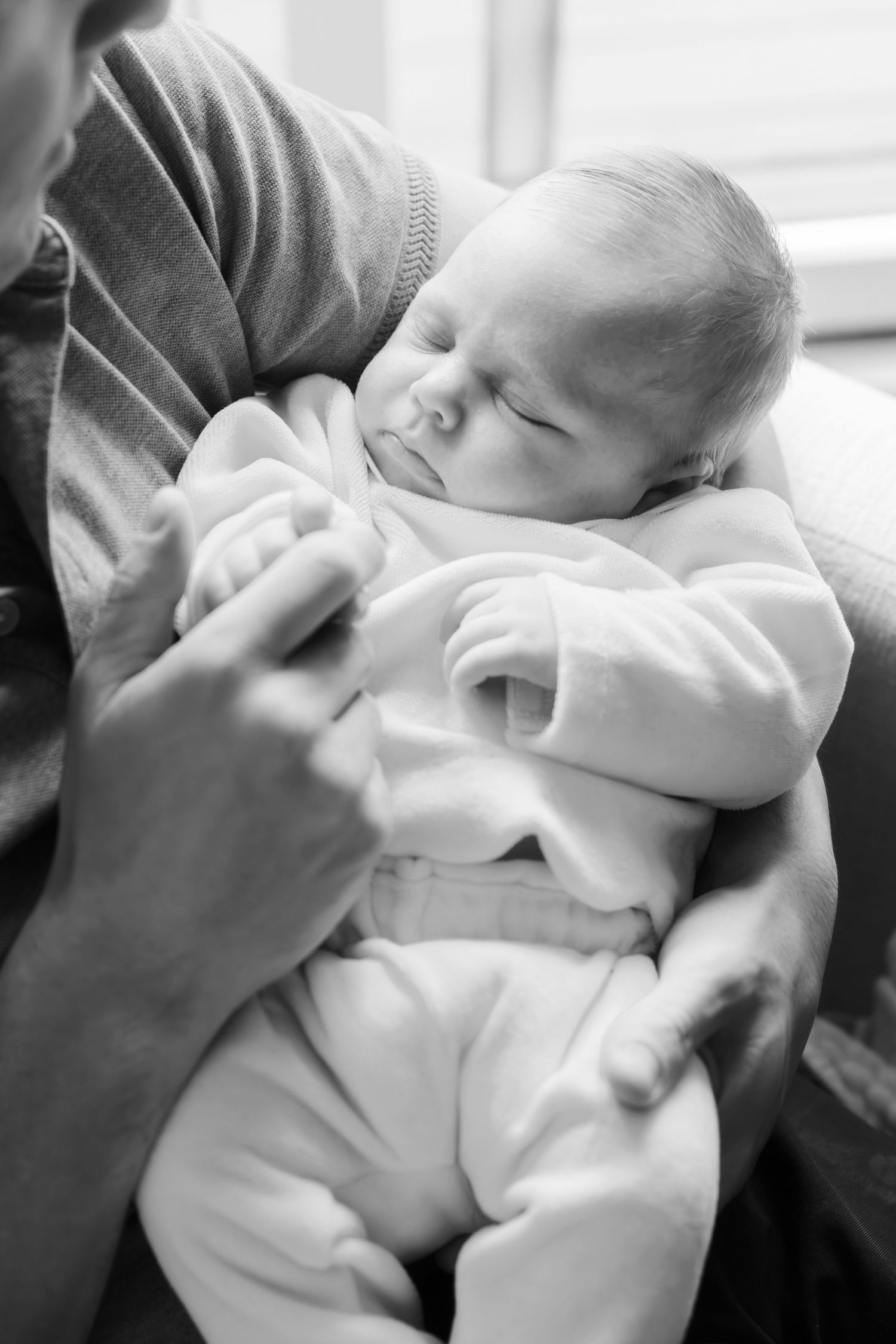 Black and white photo of a newborn baby sleeping peacefully in an adult's arms.