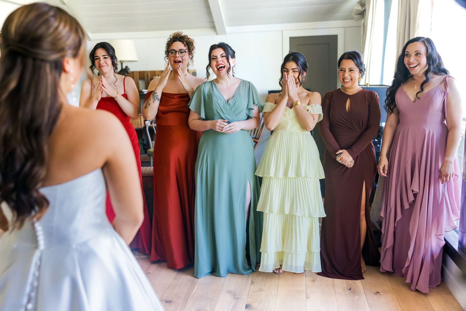 Bridesmaids in colorful mismatched gowns react with joy and tears to seeing the bride for the first time.