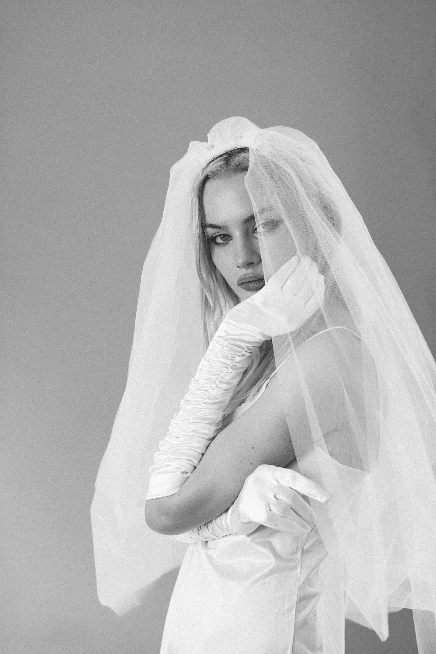 Black and white portrait of a blonde bride wearing white veil and long satin gloves.