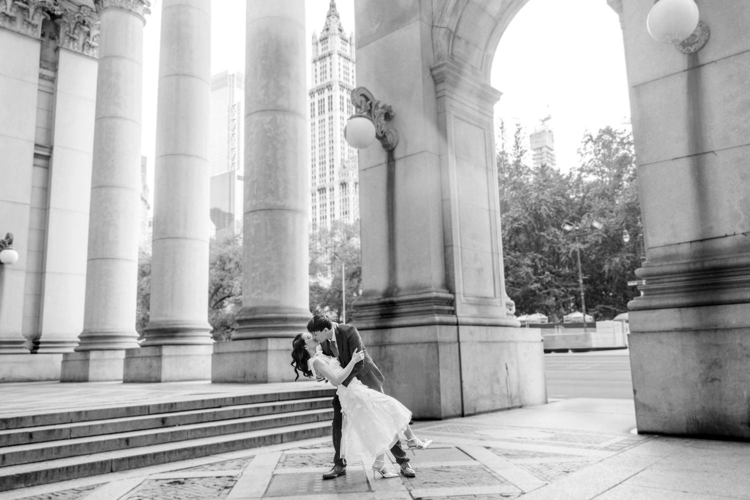 Black and white photo of bride and groom dancing between grand columns of historic building.